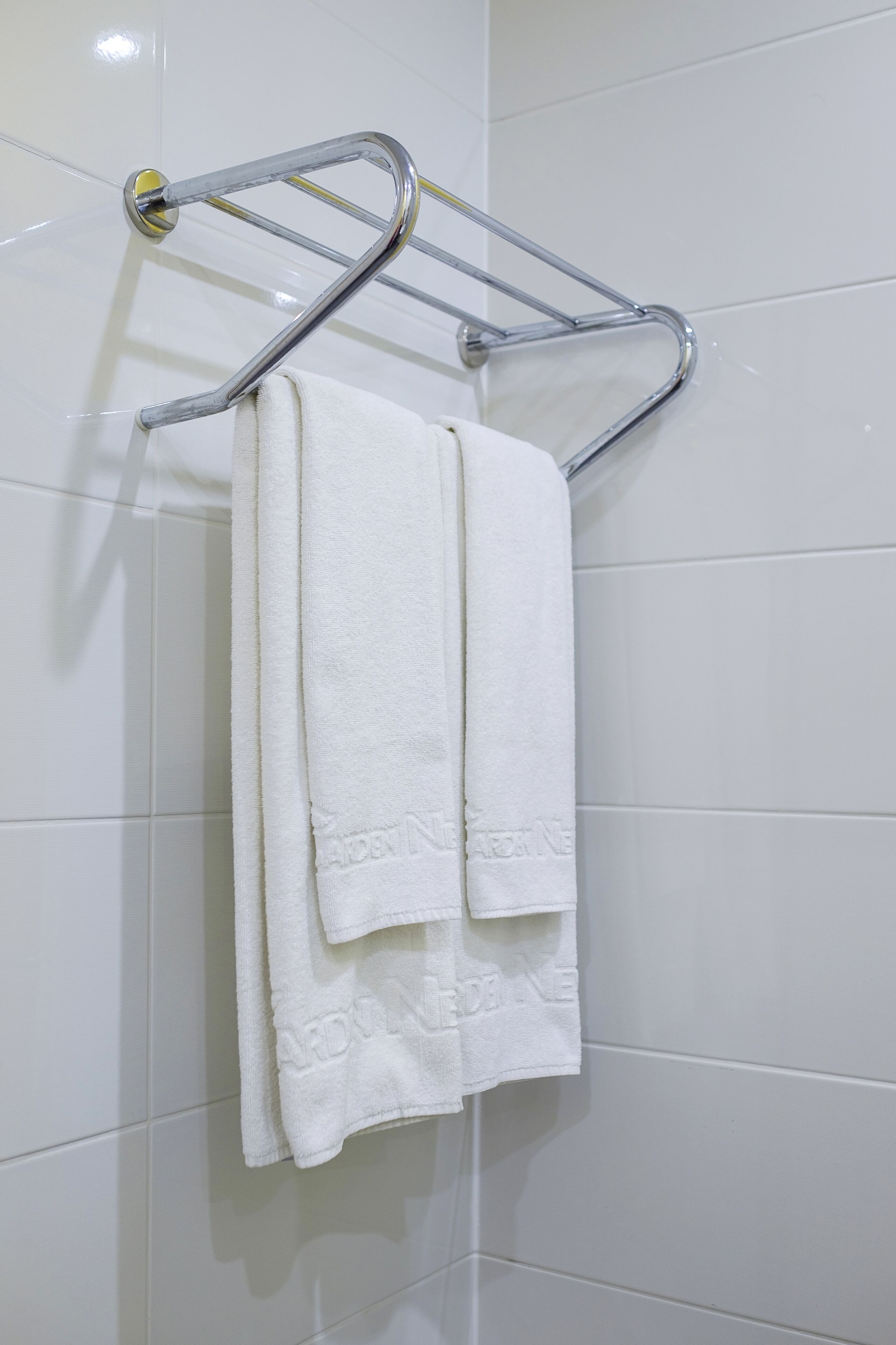 A white towel hanging on a chrome towel rack in a bathroom with white tiled walls.