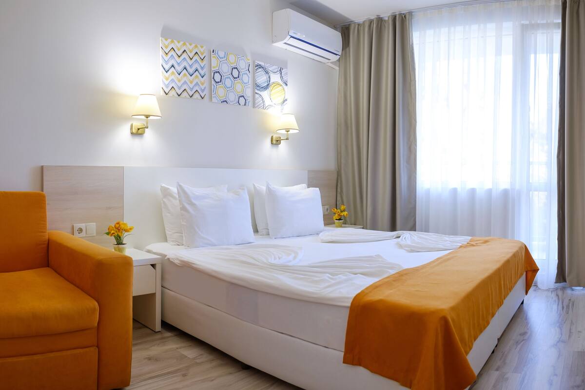 A hotel room with a large bed, a bedside table with a lamp, a chair, and artwork on the wall.