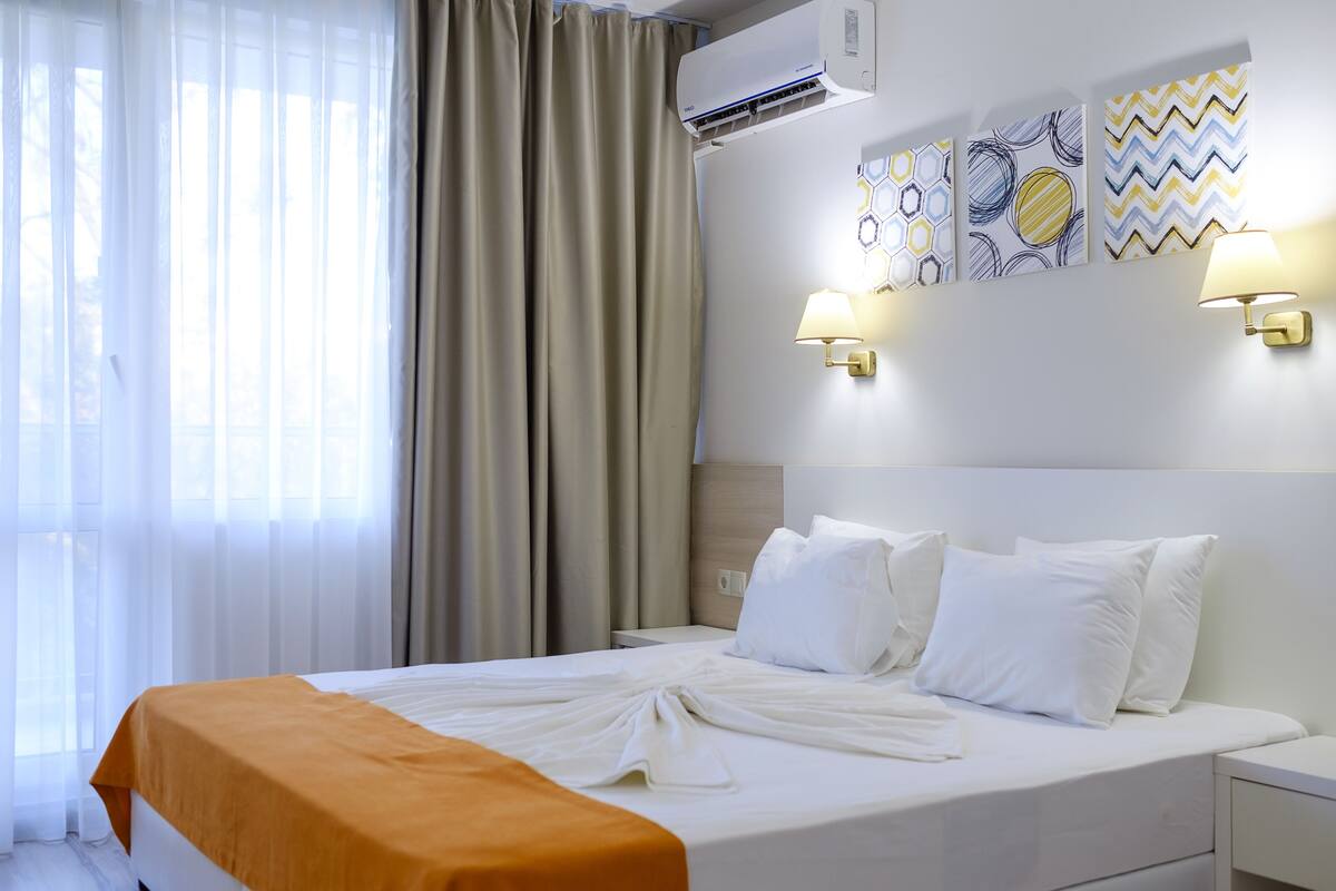 A hotel room with a bed, curtains, wall-mounted lamps, and a wall with decorative patterns.