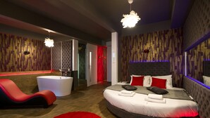 Un dormitorio moderno con una cama curva, un sillón rojo, una bañera blanca y una alfombra roja.