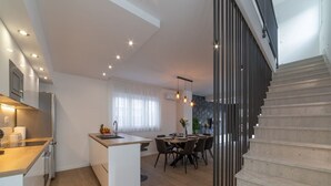 A modern kitchen with a central island, a dining area with a table and chairs, and a staircase leading to an upper level. - Luxury Villa Luna Kastela (Kaštel Stari)