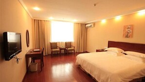 Een hotelkamer met een bed, een televisie, een bureau, een stoel en een raam met gordijnen.