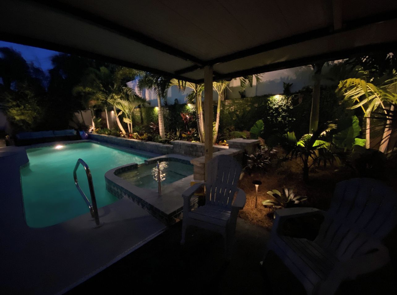 Un bain à remous avec une piscine, entouré de chaises et de palmiers, le tout abrité sous une structure.