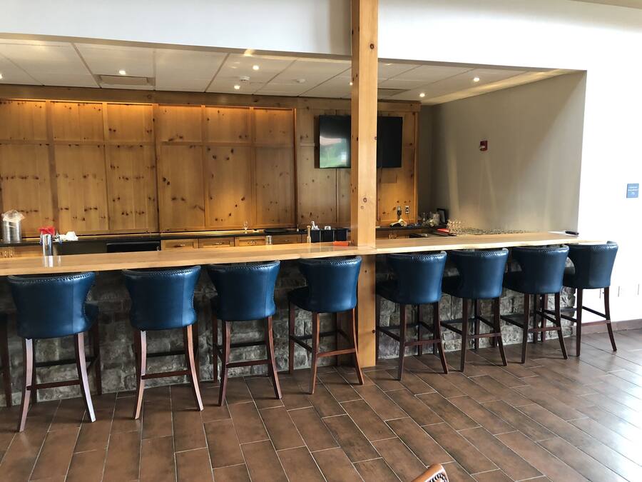 A bar area with a long wooden counter, six blue bar stools, and a stone wall backdrop.