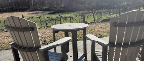 Un patio con sillas Adirondack y una mesa pequeña, con vista a un viñedo.