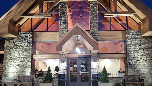Un edificio con fachada de piedra, techo de madera y una amplia entrada con puertas de cristal.