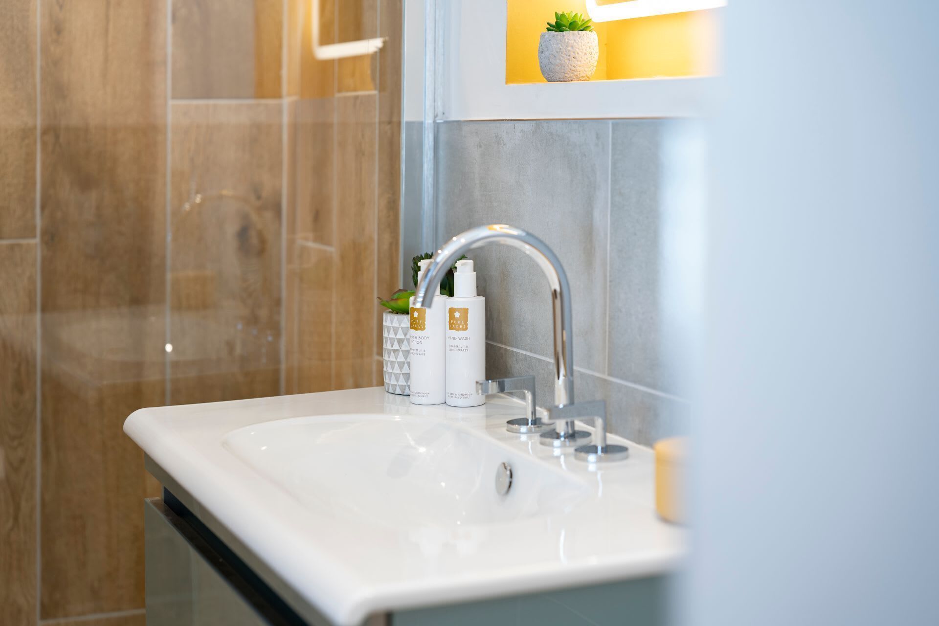 A modern bathroom with a white sink, a handheld showerhead, and two bottles of hand wash soap.