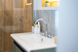 A modern bathroom with a white sink, a handheld showerhead, and two bottles of hand wash soap.