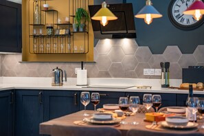 A modern kitchen with a wooden shelf, a kettle, and a dining table set for a meal.