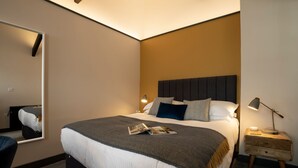Una habitación de hotel moderna con una cama grande, una mesita de noche con lámpara y un espejo en la pared.