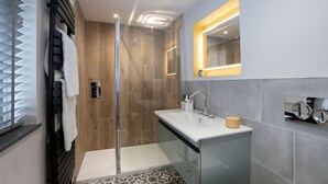 Un baño moderno con cabina de ducha de vidrio, un lavabo blanco con espejo superior y baldosas de suelo con diseño.