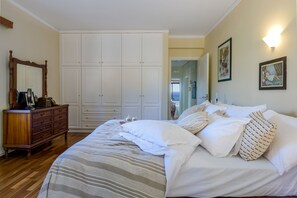 A bedroom with a large bed, a dresser, a wardrobe, and a mirror.