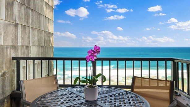 A balcony with a view of the ocean, a potted orchid, and two wicker chairs.