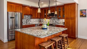 A kitchen with wooden cabinets, a stainless steel refrigerator, a marble countertop, and a central island with stools. - Pili Mai at Poipu #06E By Parrish Kauai- best Poipu location & AC - walk to shop (Koloa)