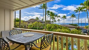 Uma varanda com mesa e cadeiras, com vista para uma área residencial com palmeiras e o oceano.
