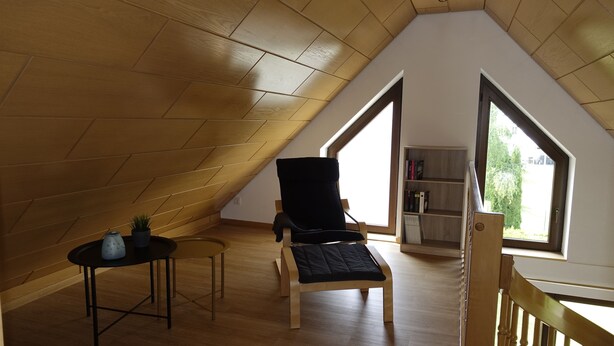 Un acogedor dormitorio en el ático, con techo inclinado, una silla negra, una mesita con una planta y una estantería.