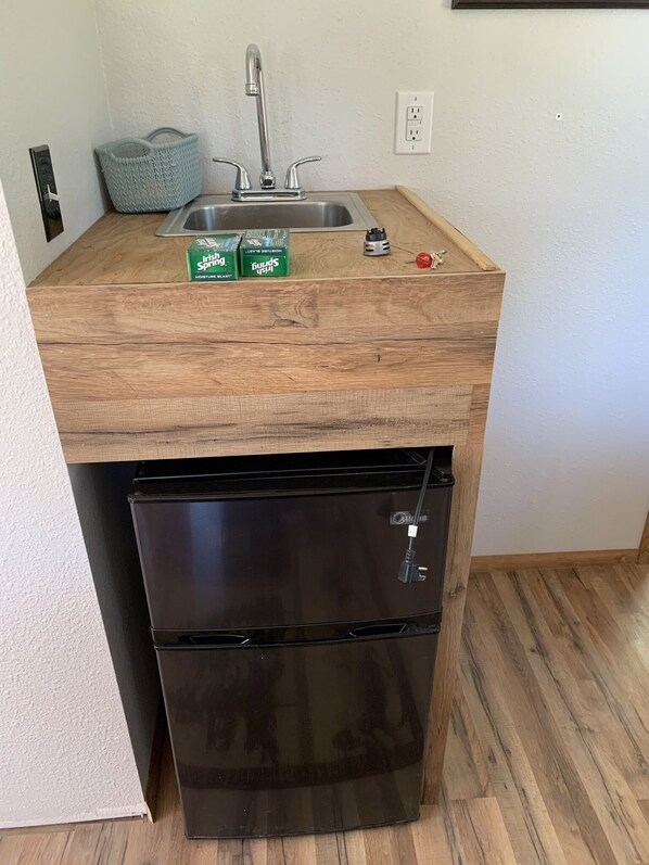 A compact kitchen with a built-in sink, a small refrigerator, and a wooden countertop.