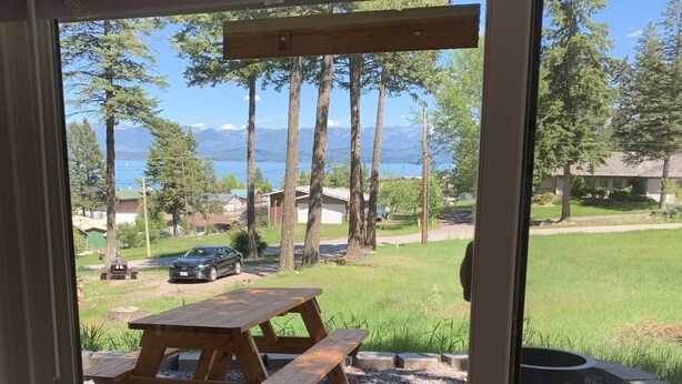 Vista a través de una ventana de un patio trasero con una mesa de picnic de madera, un pozo de fuego y un césped.