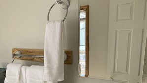 Un baño con un lavabo blanco, un espejo, un perchero con dos toallas y una botella de jabón para manos.