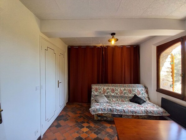 A room with a sofa, a table, a ceiling fan, and a window with curtains.