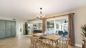Een ruime eethoek met een houten tafel en stoelen, een kroonluchter, en uitzicht op de keuken en woonkamer.