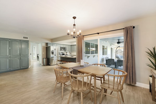 Un vaste espace dédié à la salle à manger, avec une table et des chaises en bois, un lustre, et une vue sur la cuisine et le salon.