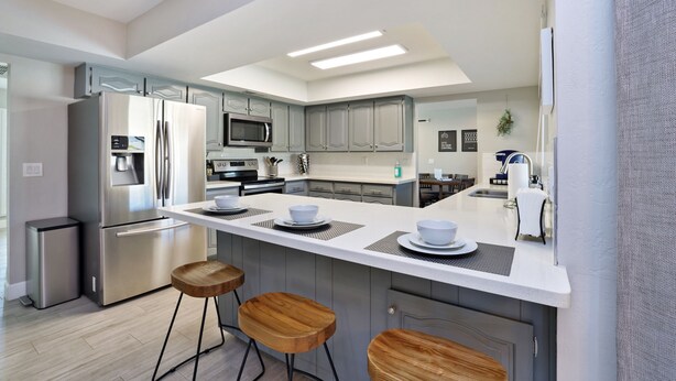Een moderne keuken met een centraal eiland, roestvrijstalen apparatuur en houten krukken.