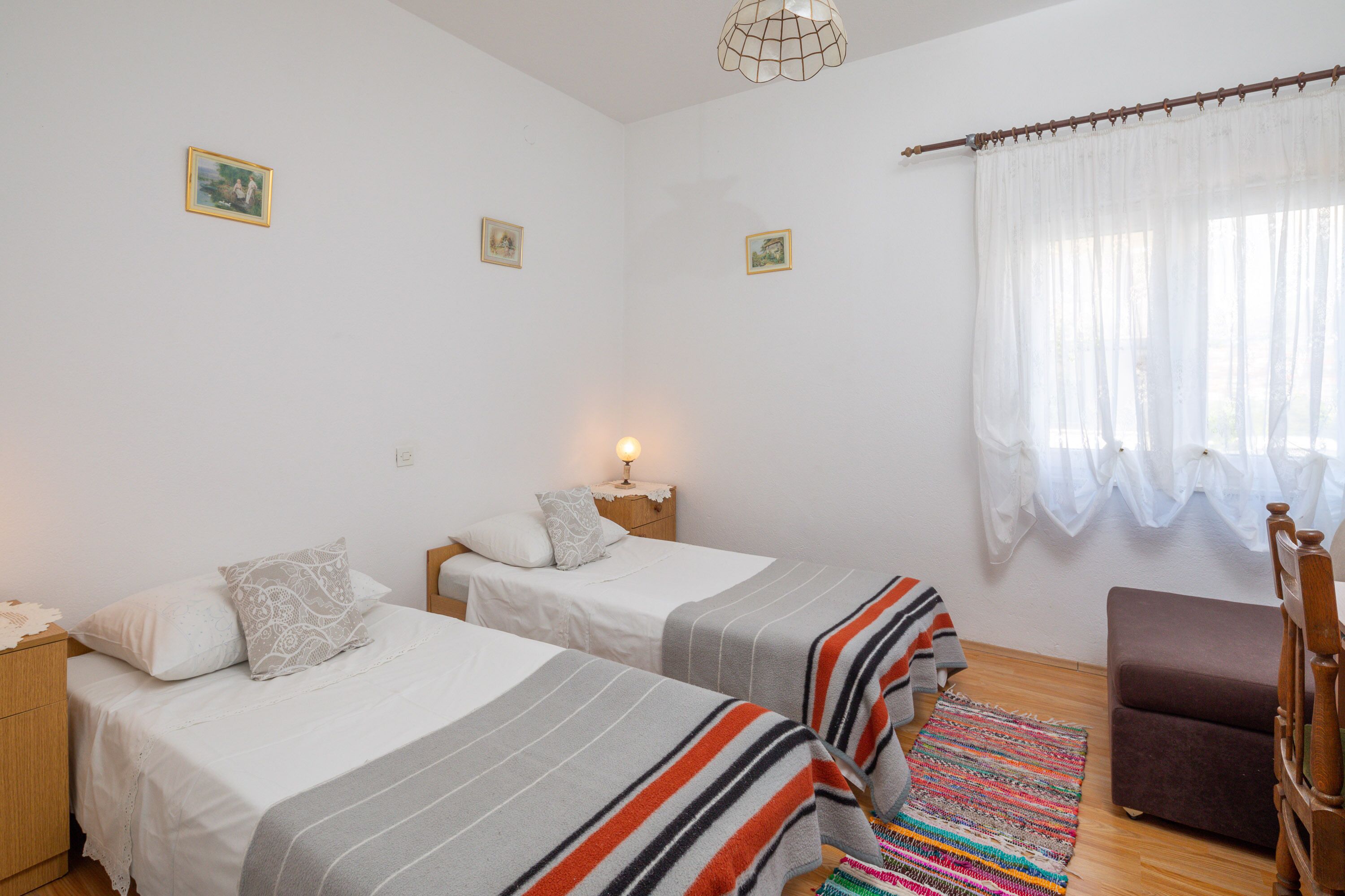 A bedroom with two beds, a nightstand, a chair, and a window with curtains.