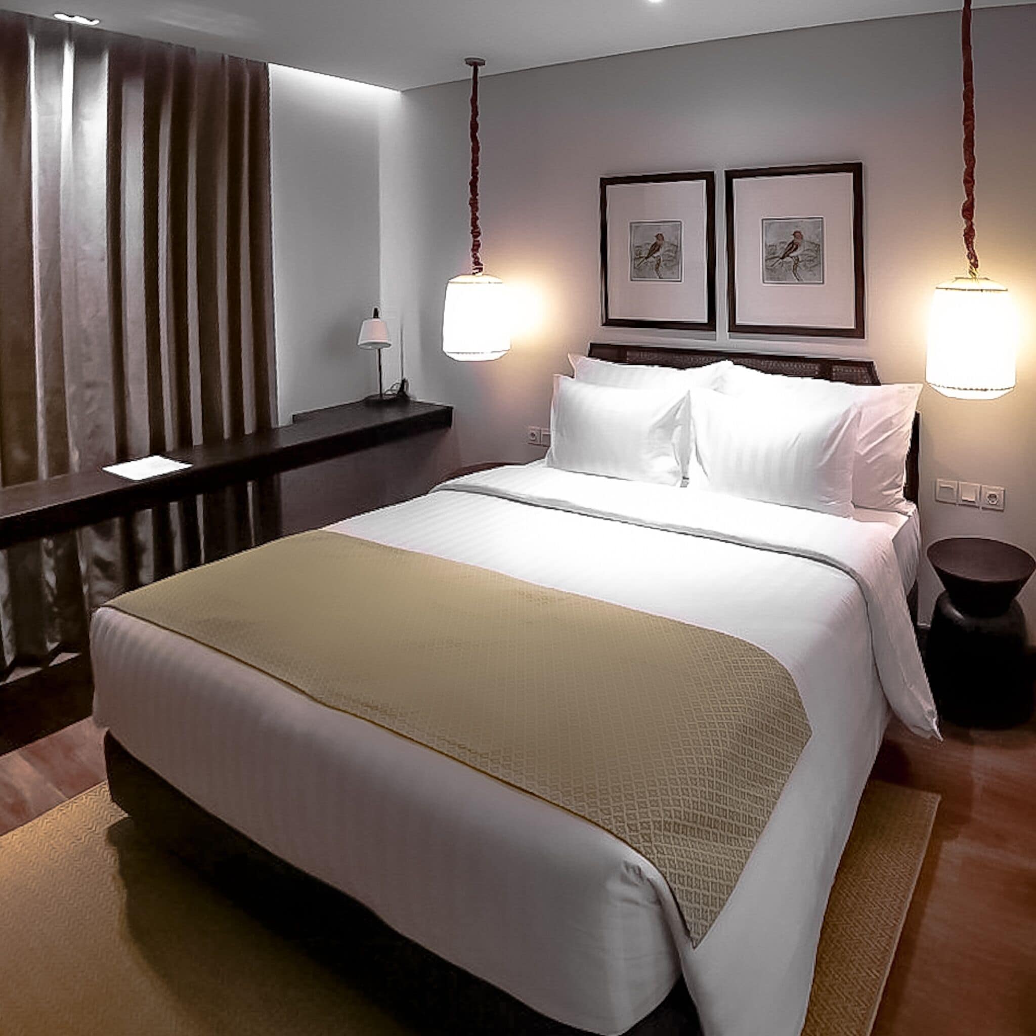 Ein Hotelzimmer mit einem großen Bett, einem Nachttisch, einer Lampe und zwei gerahmten Bildern an der Wand.