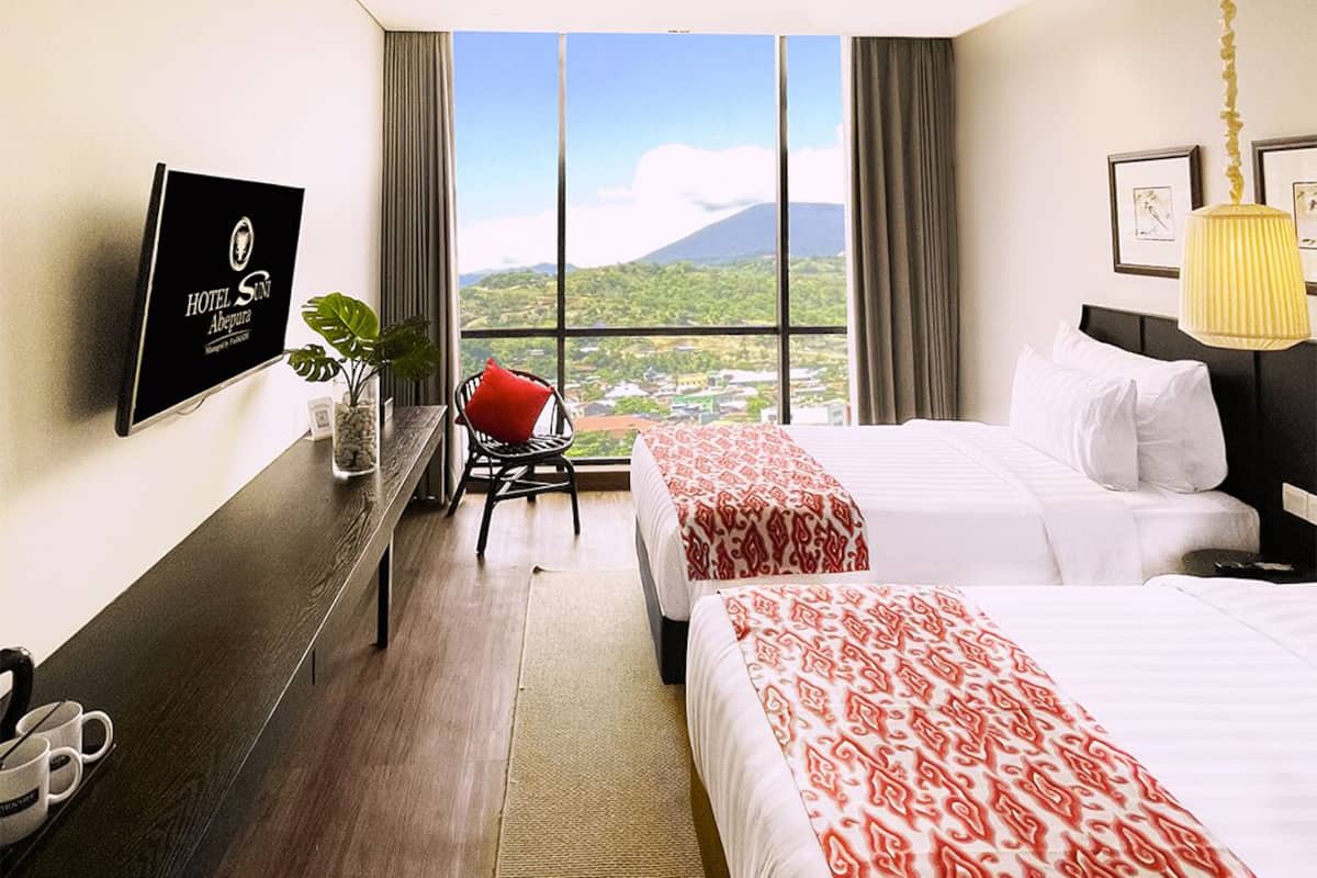 Une chambre d’hôtel avec deux lits, un bureau avec une chaise, une télévision et une vue sur une montagne.