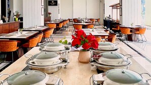 Ein geräumiger Hotel-Speisesaal mit mehreren Tischen und Stühlen, einer zentralen dekorativen Vase mit roten Blumen und einem modernen Deckenstil.