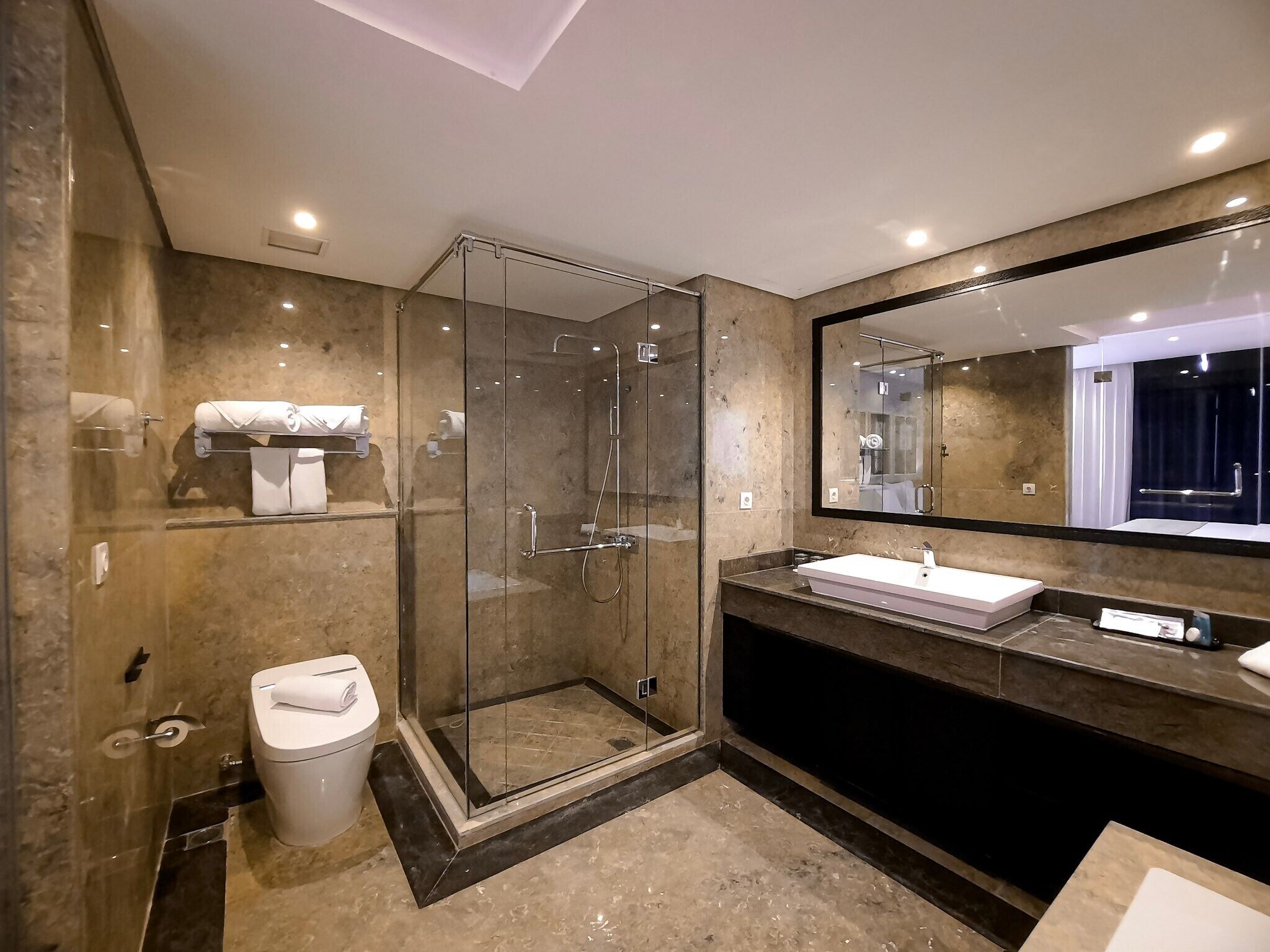 A modern bathroom with a glass-enclosed shower, a large mirror, and a vanity with a sink.