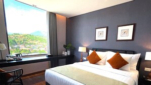 Ein Hotelzimmer mit einem großen Bett, einem Schreibtisch und Blick auf eine gebirgige Landschaft.