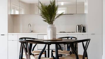 Cozinha moderna com armários brancos, uma mesa redonda para refeições com quatro cadeiras e um vaso de planta sobre a mesa.