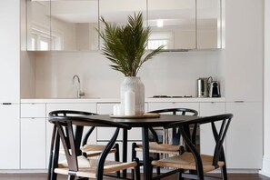Una cocina moderna con armarios blancos, una mesa redonda con cuatro sillas y una planta en la mesa.