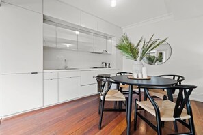 Une cuisine moderne avec des meubles blancs, une table de salle à manger ronde entourée de chaises noires et un miroir au mur.
