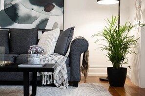 Una sala de estar moderna con un sofá gris, una mesa de centro negra y una planta grande en maceta.