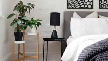 Quarto com cama, mesa de cabeceira, abajur e planta em vaso.