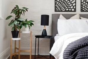 Un dormitorio con cama, mesita de noche, lámpara y planta en maceta.