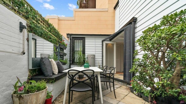 A patio with a table and chairs, surrounded by potted plants and a white wall. - Perfect Laneway Terrace, Surry Hills (Surry Hills)