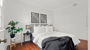 A bedroom with a bed, a nightstand, a lamp, a potted plant, and two wall art pieces. - Perfect Laneway Terrace, Surry Hills (Surry Hills)