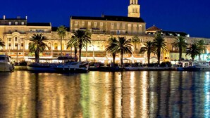 A waterfront marina with several boats docked, surrounded by historic buildings with a prominent tower. - Comfortable Modern Studio With Shaded Patio (Split)