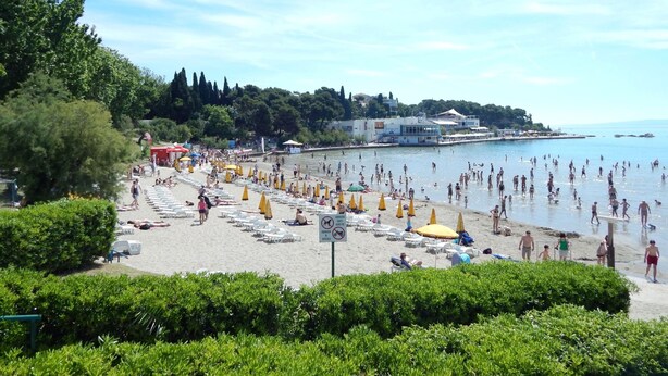 A beach with rows of sun loungers and umbrellas, a sign indicating no dogs allowed, and a view of the sea and buildings in the background. - Comfortable Modern Studio With Shaded Patio (Split)