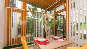 A dining area with a wooden table set for two, a glass vase with flowers, and a view of greenery outside. - Comfortable Modern Studio With Shaded Patio (Split)