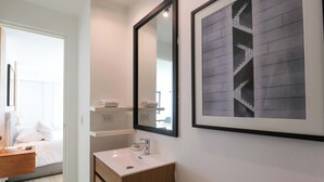 Un baño moderno con un lavamanos blanco, tocador de madera y un cuadro con una escalera.