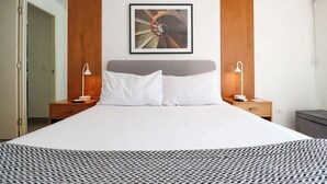 Una habitación de hotel moderna con una cama grande, paneles de madera, una obra de arte enmarcada sobre la cama y lámparas de noche.