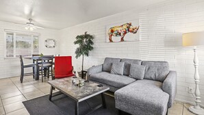 A living room with a grey sofa, a red chair, a dining table with chairs, a ceiling fan, and a wall-mounted lamp. - Pinchot Tres | Old Town Scottsdale (Scottsdale)