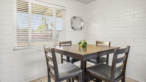 A dining area with a wooden table and four chairs, white brick walls, and a window with blinds. - Pinchot Tres | Old Town Scottsdale (Scottsdale)