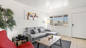 A living room with a grey sofa, red chair, and a coffee table. There is a plant, a lamp, and a painting on the wall. - Pinchot Tres | Old Town Scottsdale (Scottsdale)
