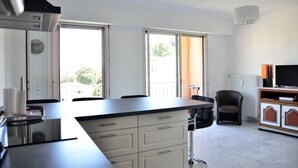 A modern kitchen with a large island, white cabinetry, and a dining area with a chair. - Quiet, Clear view, Close to Beaches and Shops, Parking & Wifi Included (Menton)